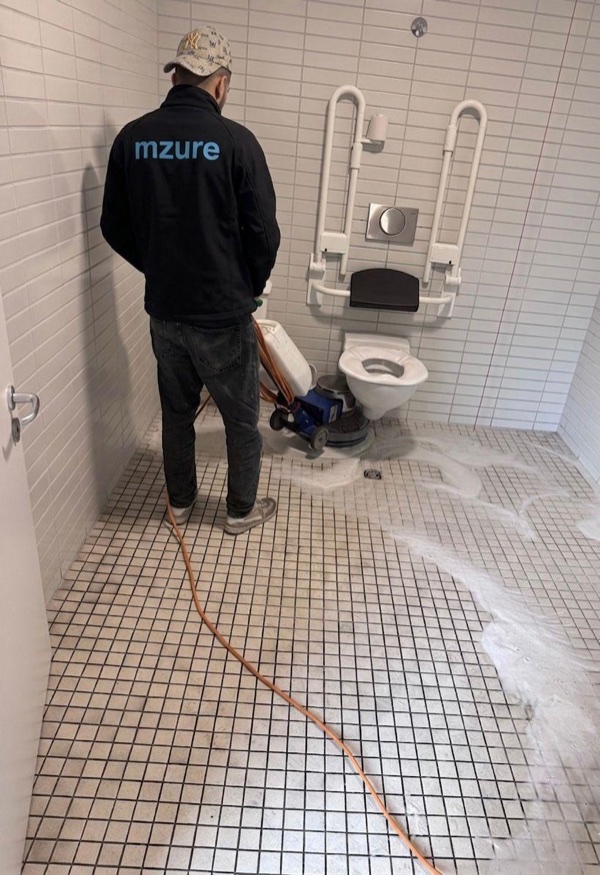 MZURE Mitarbeiter reinigt einen Sanitärbereich mit einer Einscheibenmaschine